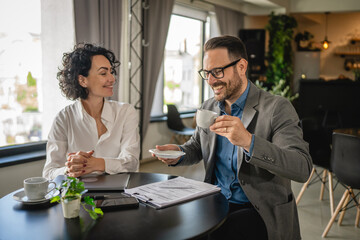 Two colleagues man and woman on break at cafe drink coffee and talk