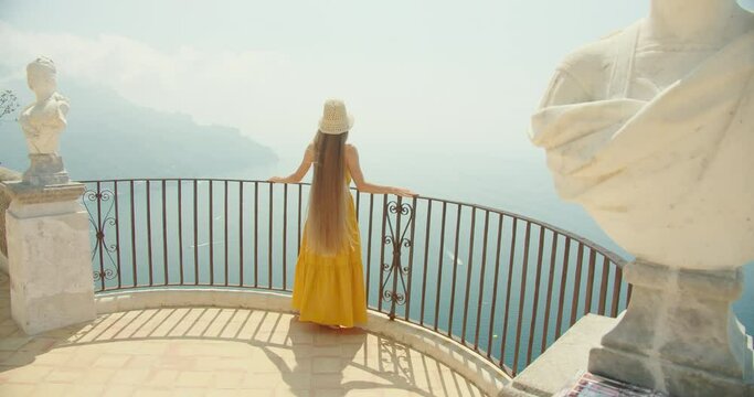 A woman gazes at the sea from a scenic overlook in Italy, with statues and ironwork on the background. Tourist on sightseeing tour in summer vacation.
