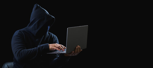 Portrait hacker spy man one person in black hoodie sitting on table looking computer laptop used login password attack security to data digital internet network system night dark background copy space