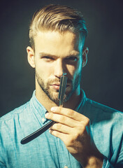 Barbershop advertising. Professional barber with straight razor. Handsome hairdresser in stylish shirt showing sharp blade of his razor. Barber shop accessories. Sexy man with vintage razor in hand.