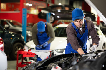 Skilled male auto mechanic in blue overalls repairing automobile in car workshop