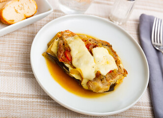 Layered eggplants with cheese and ground meat served on white circular plate.