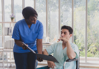 Fototapeta premium Portrait patient caucasian man sit wheelchair with woman nurse carer physical therapist African-American two people talk sign important documents advice feel relax smile happy in hospital room service