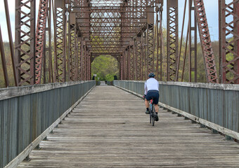 man riding a bicycle on wooden path over steel railroad trestle bridge in upstate new york (empire...
