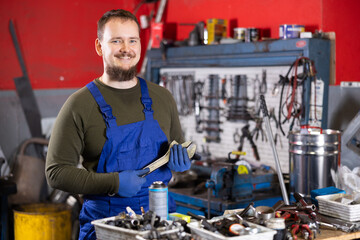 Young guy mechanic in uniform posing with wrench in car service station