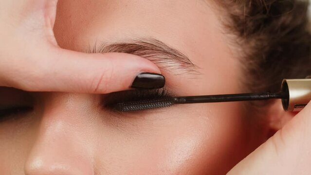 Closeup shot, style artist applies black mascara on the eyelashes of the female eye. Woman making make up using mascara. Professional makeup. Making mua. Smoky eyes makeup