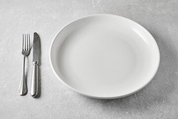 White ceramic plate with knife and fork on a gray stone table. Template for displaying food on the menu