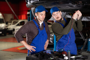 Two auto mechanics work together to diagnose an engine using a measuring device in a car service center