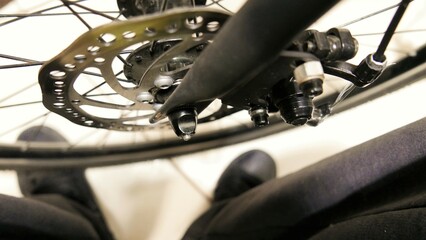 Obraz premium POV of a cyclist checking the bicycle's disc brake. A cyclist standing in front of a bike. A disc brake in details. A bike wheel.