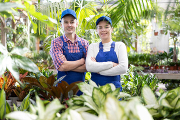 In landscaping store, garden center male and female workers in overalls stands in sales area near...