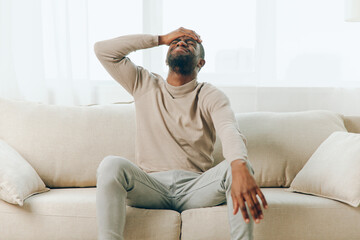 Stressed African American man with a headache sitting on the couch at home He looks tired, sick,...