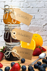 Glass jars with homemade jam decorated with a cardboard tag fixed with a string and arranged vertically one on top of the other. Homemade strawberry, orange and blueberry jam, vertical image social me