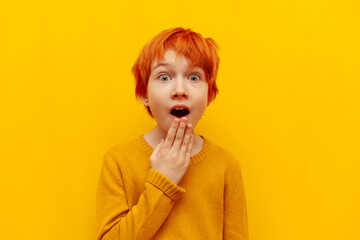 shocked red-haired teenage boy surprised and looking at camera on yellow isolated background,...