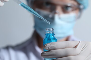 Scientist dripping liquid from pipette into glass bottle on light background, closeup