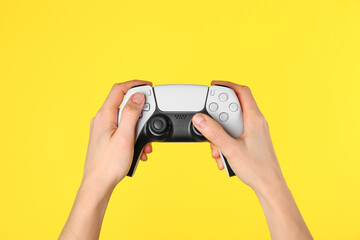 Woman using game controller on yellow background, closeup © New Africa