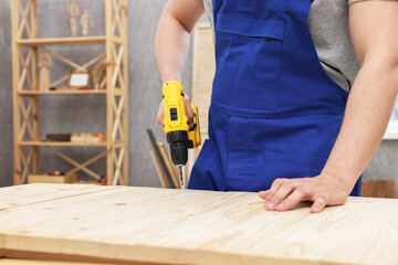 Young worker using electric drill at table in workshop, closeup