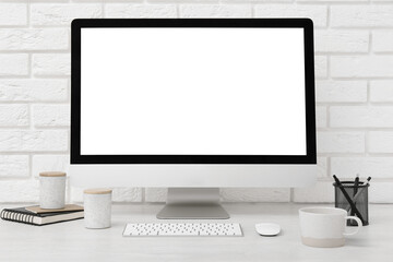 Fototapeta premium Office workplace with computer, cup and stationery on light table near white brick wall