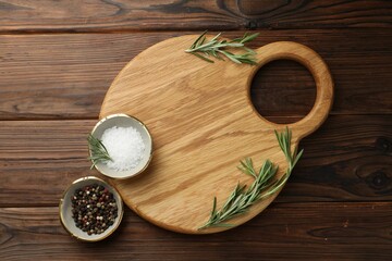 Cutting board, salt, pepper and rosemary on wooden table, flat lay. Space for text