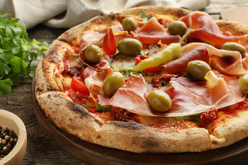 Tasty pizza with cured ham, olives, sun-dried tomato and pepper on wooden table, closeup