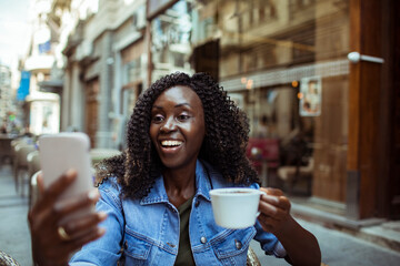 African American woman enjoying coffee and taking selfie at street cafe