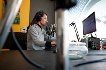 Mujer locutora en su escritorio conduciendo programa de radio FM, tez blanca, pelo negro,...