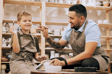 A young father and his seven-year-old son are engaged in creativity in a pottery workshop.