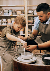 Pottering with son. Confident young man and little boy making ceramic pot on the pottery class