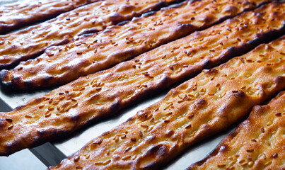 Closeup of freshly baked browned cocas with sesame seeds on steel worktable in bakery. Traditional...