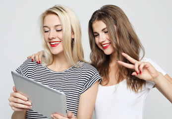 Two smiling female friends taking selfie with digital tablet over white background.