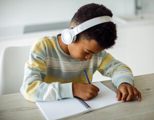 A mixed race boy writes in a notebook and listens to music on headphones