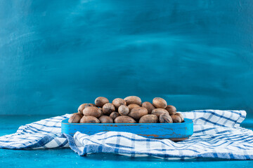 Pecan nuts in a wooden plate on a tea towel , on the blue background