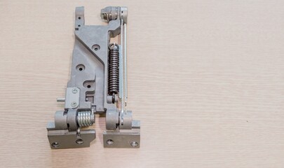 Metal hinge mechanism with a spring, viewed from above on a light wooden surface