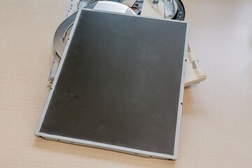 Black screen from a disassembled electronic monitor on a light wooden surface