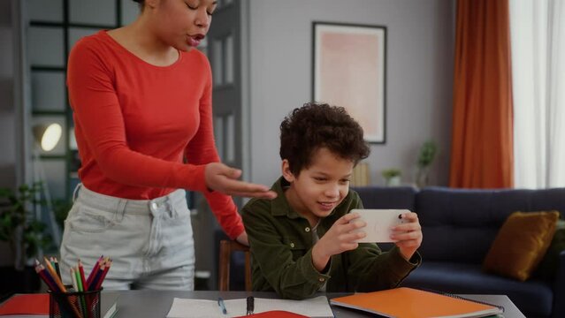 African American little boy son kid child gadget addict mobile phone game online addiction playing smartphone angry mother woman mom argue scold pick up cellphone conflict quarrel studying at home