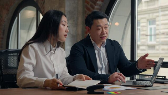 Business problem colleagues in office serious boss Asian man businessman leader male guy mentor showing mistake documents report talk laptop to stressed Japanese woman female girl businesswoman intern