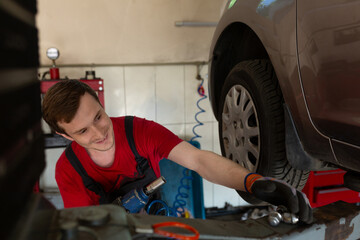 a mechanic stands by a car in a car service center. master removes a wheel from a car, repair,...