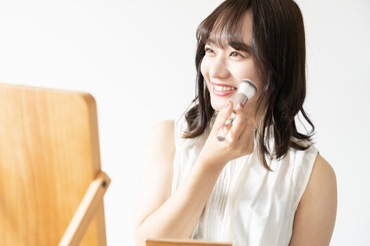 鏡を見ながらチークをブラシで塗っている笑顔の女性