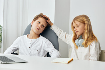 Obraz premium Happy children studying online with laptops and headphones at home in their cozy living room The boy and girl, siblings, are sitting at the table, fully concentrated on their elearning lessons The