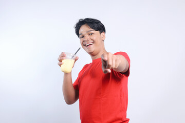 Potrait Of Happy Young Asian Guy Holding Juice Drinks And Pointing At Camera Isolated On White...