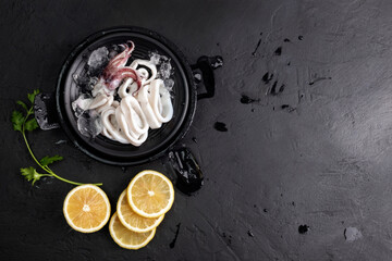 Fresh raw squid. Sliced ​​raw squid placed on a black plate with ice, lemon slices. Top view...