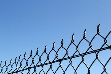 Section of a chain link fence against a clear blue sky