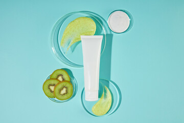 Mock up for promote with a sample cosmetic tube displayed between two glass platforms, next to a dish of fresh kiwi. Scrubs of kiwi helps skin increase elasticity, firmness, and shine