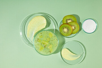 Top view photography over light green background, plenty glass pedestals with exfoliation cream and fresh kiwi displayed above. Vacant space for designing or adding text