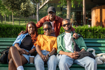 Four satisfied african american stylish friends resting on bench in park looking at camera...
