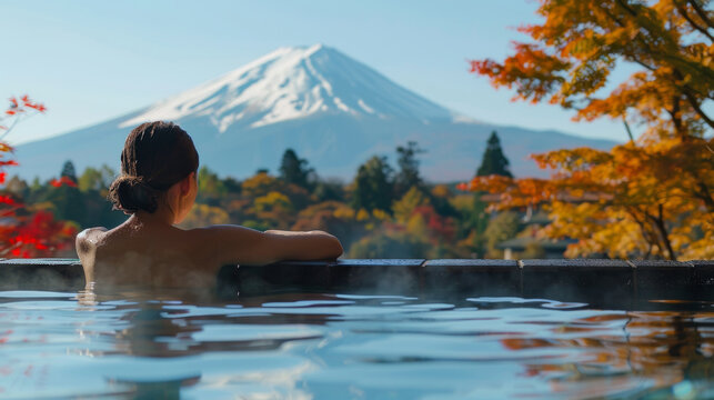 Woman relaxing in hot springs onsen and enjoying Fuji mountain view with red maple leaves in autumn