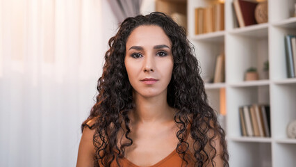 Female portrait. Confident expression. Calm pretty woman with serious face dark curly hair at light...