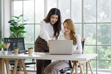 Two asian women working on laptop computer with a coffee cup, mobile phone and document folder at a...