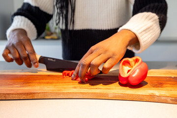 This close-up image captures the hands of a Black woman as she skillfully chops a red bell pepper...