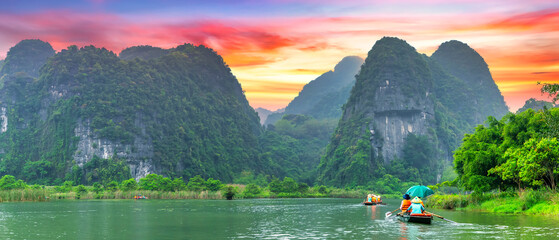 Ninh Binh, Vietnam - April 5th, 2024: Tourists float by boat on the river of the Tam Coc National Park Sightseeing tour to grottoes with sunset sky, Ninh Binh, Vietnam.