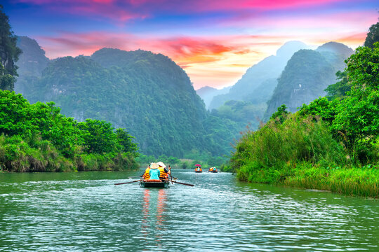 Ninh Binh, Vietnam - April 5th, 2024: Tourists float by boat on the river of the Tam Coc National Park Sightseeing tour to grottoes with sunset sky, Ninh Binh, Vietnam.